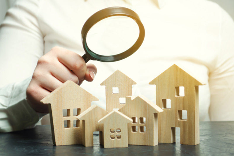 Immobilienmakler Neu Isenburg hält eine Lupe über mehrere kleine Holzhäuser um die Immobilien zu bewerten
